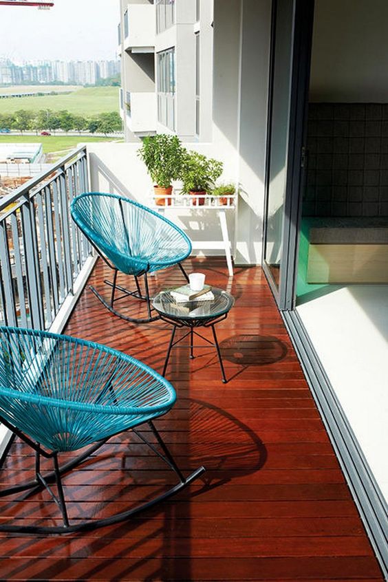 Balcon deschis cu pardoseala din lemn lacuit parapet metalic si scaune albastre din fire intinse cu masa de cafea rotunda din sticla