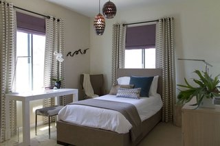 Dormitor mic cu pat pe mijloc si birou si cu draperii cu model la fereastra