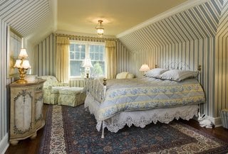 Dormitor clasic cu pat din fier forjat alb si tapet pe pereti in dungi gri bleu cu alb si maro